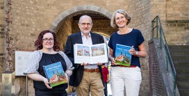 drei Personen mit der Publikation in den Händen vor einer Mauer, im Hintergrund ein Teil des Xantener Doms