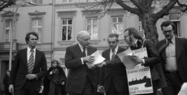 mehrere Männer im Gespräch mit einem Demonstranten, der ein Schild umgehängt trägt